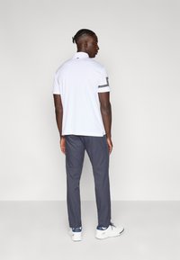 Polo blanco con cuello y mangas cortas, combinado con pantalones gris oscuro. Presenta un patrón a rayas en las mangas y zapatos deportivos blancos.