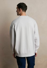 Jasnoszary, luźny sweter z dzianinowymi mankietami i dołem, o miękkiej teksturze, z okrągłym dekoltem i obniżonymi szwami na ramionach.