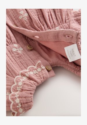 Roza bombažna obleka s teksturirano tkanino, belo cvetlično vezenino, valovitim robom in lesenimi gumbi. Oznaka pravi "NEXT baby, izdelano v Indiji."