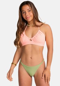 Dvoudílný bikinový set s ribovaným broskvovým bikinovým topem a předním výřezem a zelenými pruhovanými bikinovými kalhotkami s nízkým pasem. Hladká textura.
