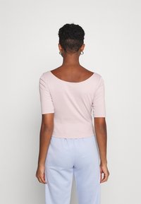 Vaaleanpunainen lyhythihainen crop-top, jossa on leveä pääntie, yhdistettynä vaaleansinisiin housuihin. Pintamateriaali on sileää ja muotoilu yksinkertaista.