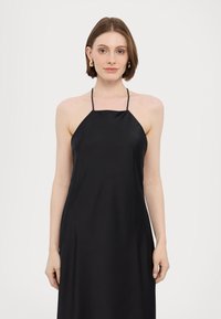 Black satin halter dress with a loose fit, featuring thin straps and a smooth texture. Length reaches just above the ankles.