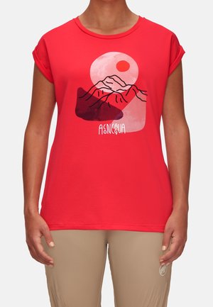 Chemise rouge à manches courtes avec poignets retroussés présentant un motif de montagne et de soleil et le mot "Asinegua", portée avec un pantalon beige.