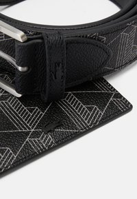 Cinto de couro preto com um padrão geométrico em prata, com uma fivela de metal prateada e um detalhe de logotipo na correia. Acabamento de superfície texturizada.