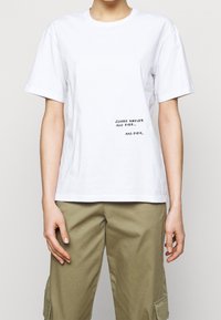 Hvid bomulds t-shirt med korte ærmer og rund halsudskæring. Har sort tekst med teksten "LUKKET FOR EVIGT OG ALDRIG... OG ALDRIG."