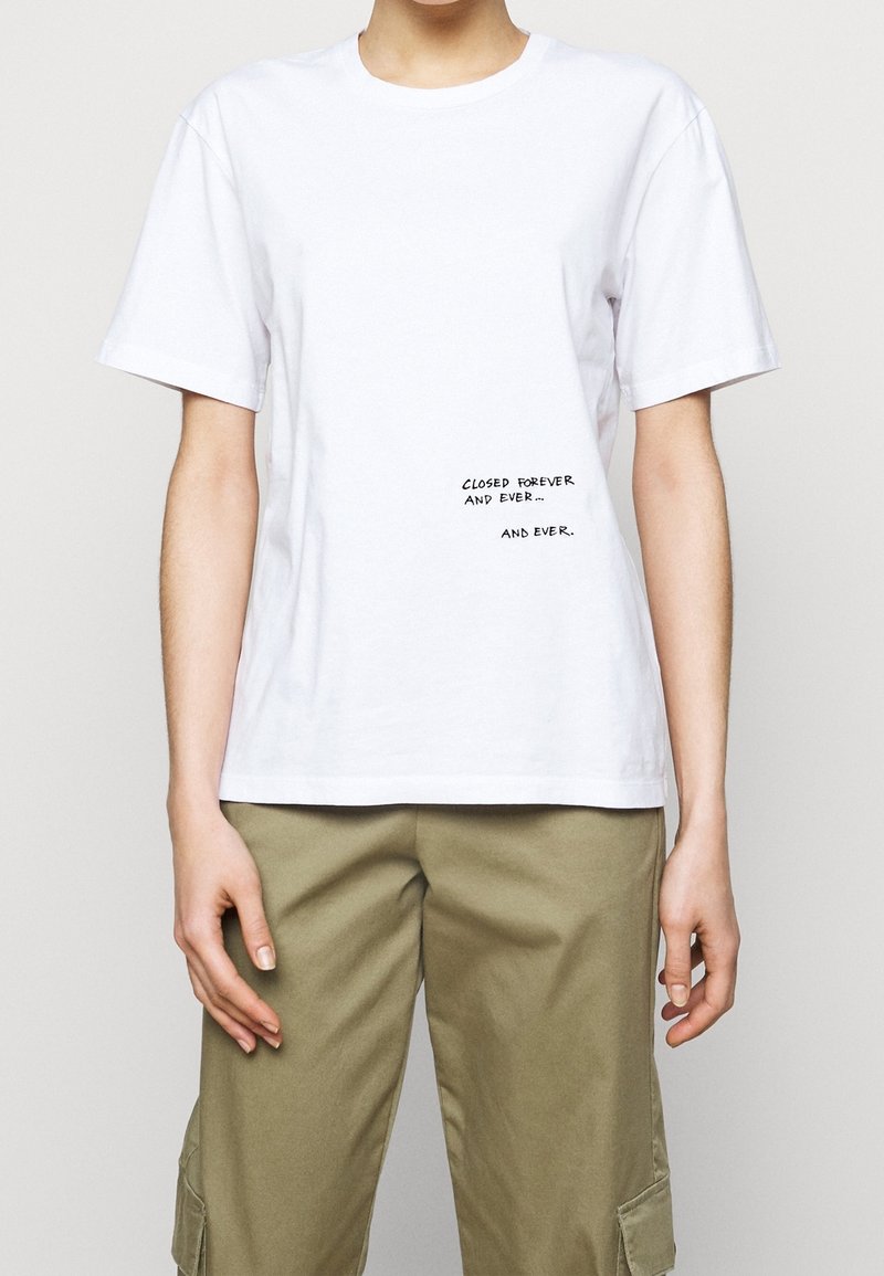 Hvid bomulds t-shirt med korte ærmer og rund halsudskæring. Har sort tekst med teksten "LUKKET FOR EVIGT OG ALDRIG... OG ALDRIG."