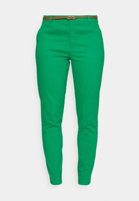 Zielone spodnie z wysokim stanem, zwężające się ku dołowi, z wąskim brązowym paskiem z srebrną klamrą.