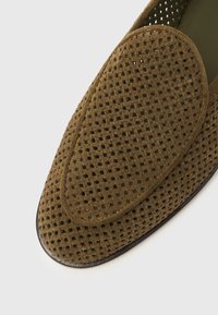 Καφέ σουέντ μοκασίνι με διάτρητο σχέδιο, στρογγυλεμένη μύτη και λείο μαύρο πέλμα. Διαθέτει απαλή υφή και αναπνεύσιμο υλικό.
