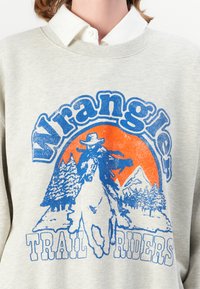 Svetlošedá mikina s modrou grafikou cowboya na koni proti oranžovému západu slnka, s textom "Wrangler Trail Riders".