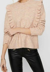 Jasnoróżowy dzianinowy sweter z falbankami na ramionach i prążkowanym dołem. Połączony z czarnymi skórzanymi spodniami z detalami na suwakach.