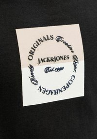 Czarny bawełniany t-shirt z kwadratową kremowo-beżową naszywką z granatowym haftowanym napisem i logo, wskazującym markę i lokalizację.