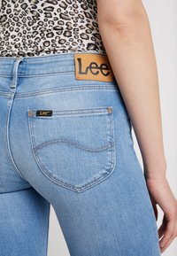 Jeans de denim azul claro con una etiqueta de cuero de Lee en la cinturilla, que cuentan con dos bolsillos traseros y detalles de costura en contraste.