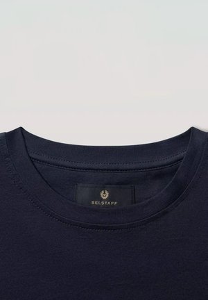 Primo piano di una t-shirt blu navy con scollo a girocollo che mostra l’etichetta del marchio Belstaff cucita all’interno del colletto.