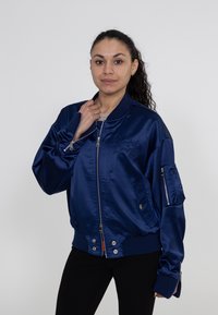 Marineblaues Satin-Bomberjackett mit Reißverschluss vorne, gerippten Bündchen, Seitentaschen und einer Reißverschlusstasche am Arm mit gesticktem Logodetail.