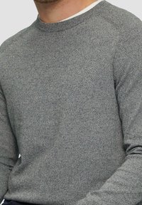 Szary sweter z dzianiny z okrągłym dekoltem i ściągaczami na rękawach. Materiał ma subtelną fakturę, z wzorem mieszanym ciemnoszarym i jasnoszarym.