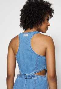Denim jurk met een mouwloos ontwerp, lichtblauwe kleur, uitsparingen aan de zijkanten en een ceintuur in de taille. Heeft een ronde halslijn en een gemêleerde stof.