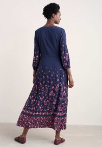 Dunkelblaues Blumen Kleid mit langen Ärmeln, das rosa Blumenmuster und einen gestuften Saum aufweist. Der Stoff ist leicht und hat eine fließende Silhouette.