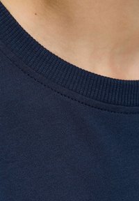 Detailní záběr na námořnickou tkaninu s texturovaným žebrovaným límcem, který zdůrazňuje jemnost a detaily šití. Vedle je viditelná hladká pleť.