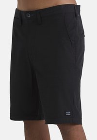 Shorts neri realizzati in tessuto morbido, caratterizzati da una parte anteriore piatta, passanti per cintura e tasche laterali. Include una piccola etichetta con logo vicino all'orlo.