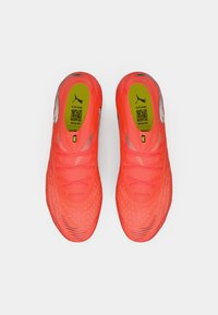 Jasne neonowo-pomarańczowe buty piłkarskie o teksturowanej powierzchni, z cienkimi sznurowadłami i czarnymi akcentami na podeszwie. Zawierają logo Puma oraz etykietę z kodem QR.