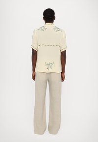 Camisa de manga corta de color amarillo claro con bordado floral, de corte relajado. Combinada con pantalones de pierna ancha en color beige, creando una silueta suelta.