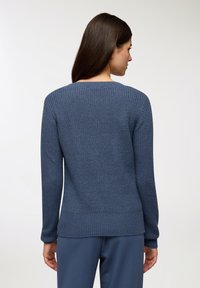 Niebieski sweter robiony na drutach z teksturowanym wzorem, okrągłym dekoltem oraz ściągaczami na mankietach i dolnej krawędzi. Prezentowany od tyłu z długimi rękawami.