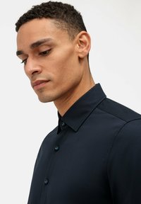 Camicia button-up blu scuro con colletto strutturato, presenta un tessuto liscio e bottoni blu. Ha una silhouette aderente.