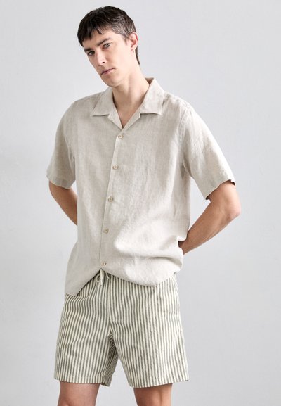 Camicia a maniche corte in lino beige chiaro con colletto a pieghe e chiusura a bottoni, abbinata a pantaloni corti a righe chiare con vita elasticizzata.