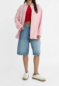 Camisa de mezclilla rosa de gran tamaño, top corto rojo, pantalones cortos bermuda de mezclilla azul y zapatillas blancas con acentos en negro y marrón.