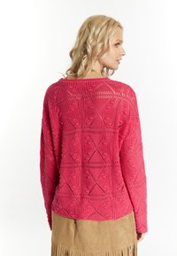 Rosa gestrickter Pullover mit einem offenen Design und geometrischen Mustern; lange Ärmel und lockere Passform. Strukturiertes Garn mit einer leicht unebenen Oberfläche.