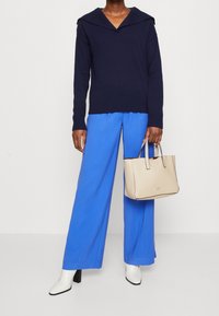 Navy knitted sweater with a wide collar, blue wide-leg trousers, and a beige leather tote bag. White high-heeled boots complete the outfit.