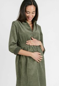 Olijfgroen corduroy jurk met een kraag, elastische tailleband en driekwart mouwen. De ribbeltextuur verbeterd de visuele diepte.