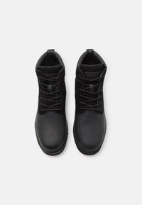 Botas negras de tobillo que presentan una combinación de cuero suave y ante, con una punta redondeada, corte alto y un diseño tradicional de cordones.