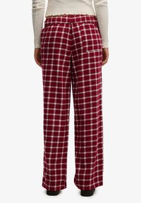 Czerwono-białe spodnie w kratkę z elastycznym pasem, szerokimi nogawkami i pojedynczą kieszenią z tyłu, wykonane z miękkiego, ciepłego materiału.