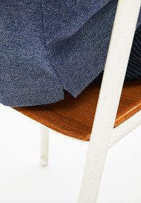 Džínová bunda přehozená přes dřevěnou židli s hladkým, teplým povrchem a bílým, mírně opotřebovaným kovovým rámem.