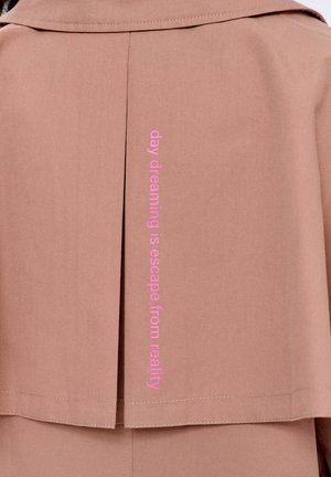 Zadní strana světle hnědého kabátu s růžovým vertikálním textem, který říká "denní snění je útěk od reality."