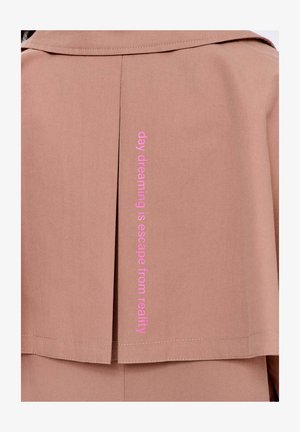 Chrbát svetlohnedého kabáta s ružovým vertikálnym textom "snívanie je únik z reality."