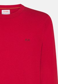Maglione rosso a maglia con collo rotondo e maniche lunghe, caratterizzato da un piccolo logo nero sul petto. Tessuto morbido e colletto a costine.