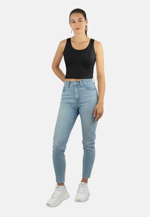 Schwarzes, kurzes Tanktop, hellblaue, hochtaillierte Jeans und weiße Sneakers. Glattes Material, figurbetontes Design und lässige Silhouette.