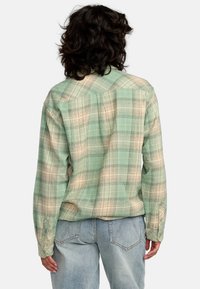 Camicia in flanella a quadri verde e beige con yoke posteriore, polsini con due bottoni e un tocco morbido. Abbinata a jeans in denim azzurro chiaro.