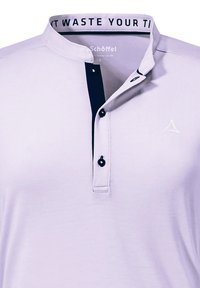 Lichtpaarse polo met een marineblauwe knoopsluiting, vijf knopen en een wit logo nabij de kraag. Heeft een opstaande kraag en een zachte textuur.