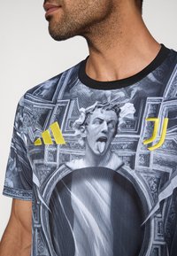 Κοντομάνικο γραφικό μπλουζάκι με μαύρο και λευκό στάμπα που περιλαμβάνει κεντρικό σχέδιο γλυπτού, κίτρινες λεπτομέρειες και μαύρο λαιμό.