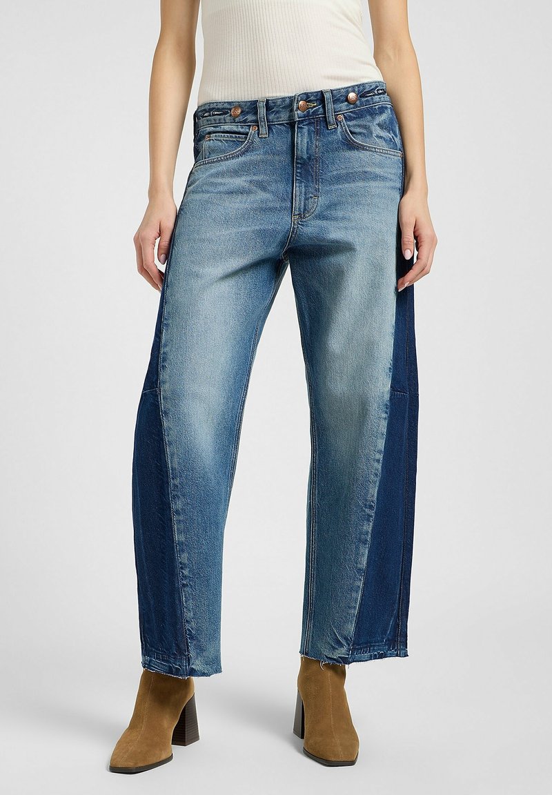 Jean en denim bleu clair avec une coupe décontractée, présentant un panneau bleu foncé sur le côté, un design à cinq poches et des accents de boutons en cuivre.