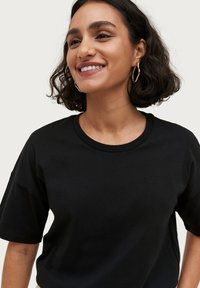 Sort kortærmet t-shirt i bomuld med rund halsudskæring og løs pasform, der har en glat tekstur og minimalistisk design.