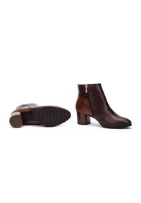 Bottes en cuir marron à la cheville avec un talon texturé et une fermeture éclair sur le côté. Présentent une finition lisse et un bout légèrement pointu.