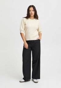 Kremveidīga ribota adīta džemperis ar īsām pūkām, apvienota ar brīvām melnām biksēm un baltām kedām ar pelēkām akcentiem.