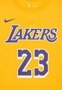 Geltonas medvilnės marškinėliai, kuriuose raudona spalva užrašas "LAKERS" purpurine spalva ir numeris "23" su baltu apvadu ir taškiniais raštais. Nike logotipas ant peties.