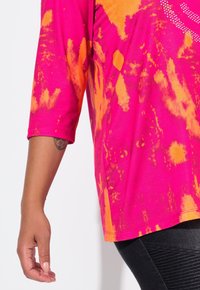 Kurzärmliges pinkes Batik-Oberteil mit orangefarbenen Akzenten, das einen lockeren Schnitt und einen runden Ausschnitt aufweist. Aus glattem Baumwollmaterial.