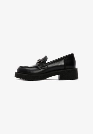 Mocassins en cuir noir avec une finition brillante, dotés d'une boucle décorative, d'une semelle épaisse texturée et d'un petit talon carré.