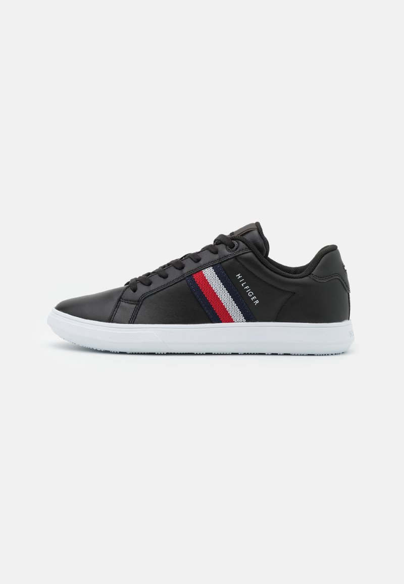 Baskets basses noires avec semelle blanche, détail en tissu rayé rouge, blanc et bleu, et texte "Hilfiger" sur la partie latérale.